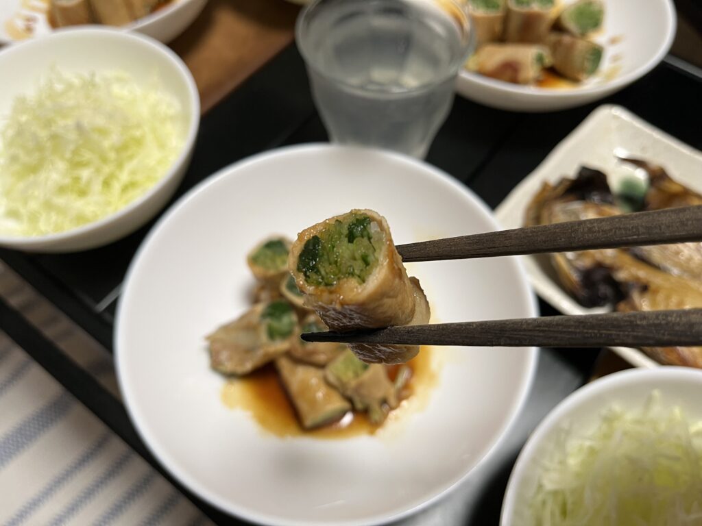 水菜の肉巻きをひとつつまんで口へ運ぶ様子