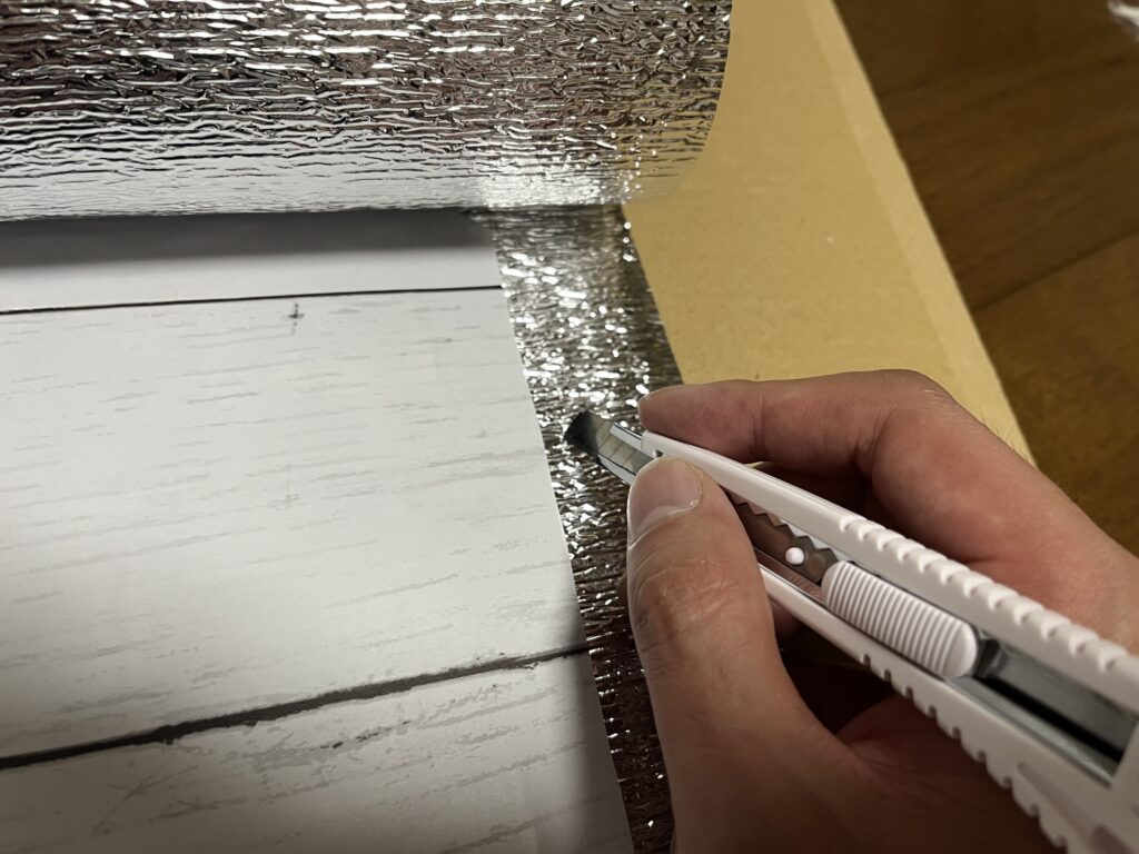 貼り付けたアルミ保温シートを1cm程度カラーボードより大きくカットしている様子