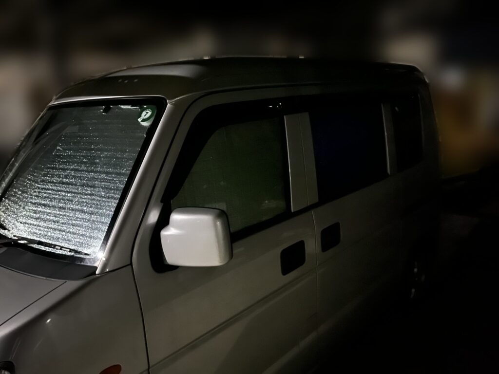 100均DIYサンシェードを装着したエブリイを夜間に外側から見て、車内の光漏れがほとんどないことを確認している様子