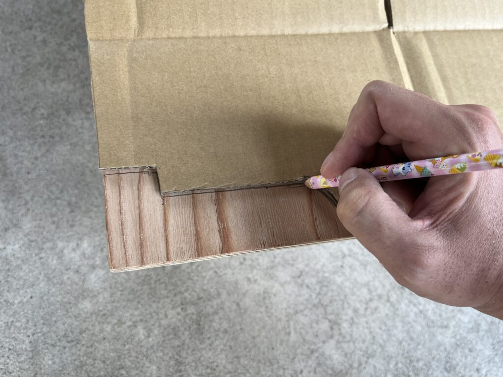 床材にダンボール型でジグソーで切り取るラインをマーキングしている様子