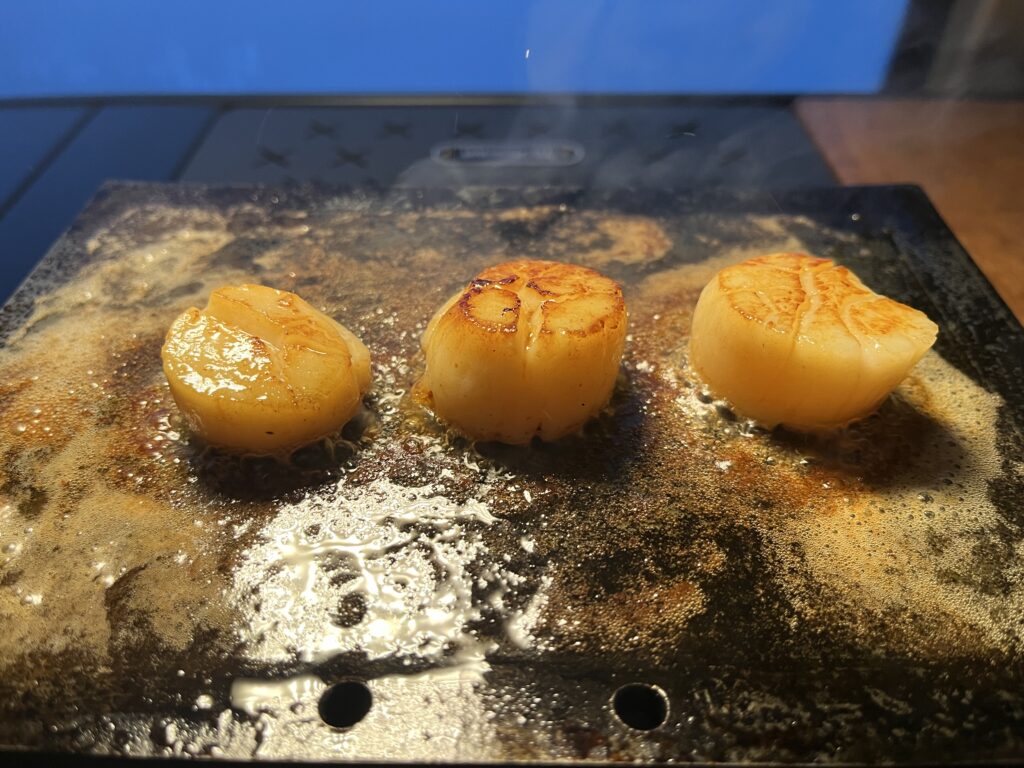 鉄板の上でほたて貝柱をバター醤油で焼いている様子