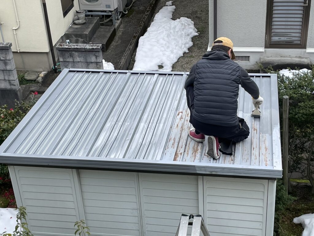 物置の屋根を1回目塗装している様子