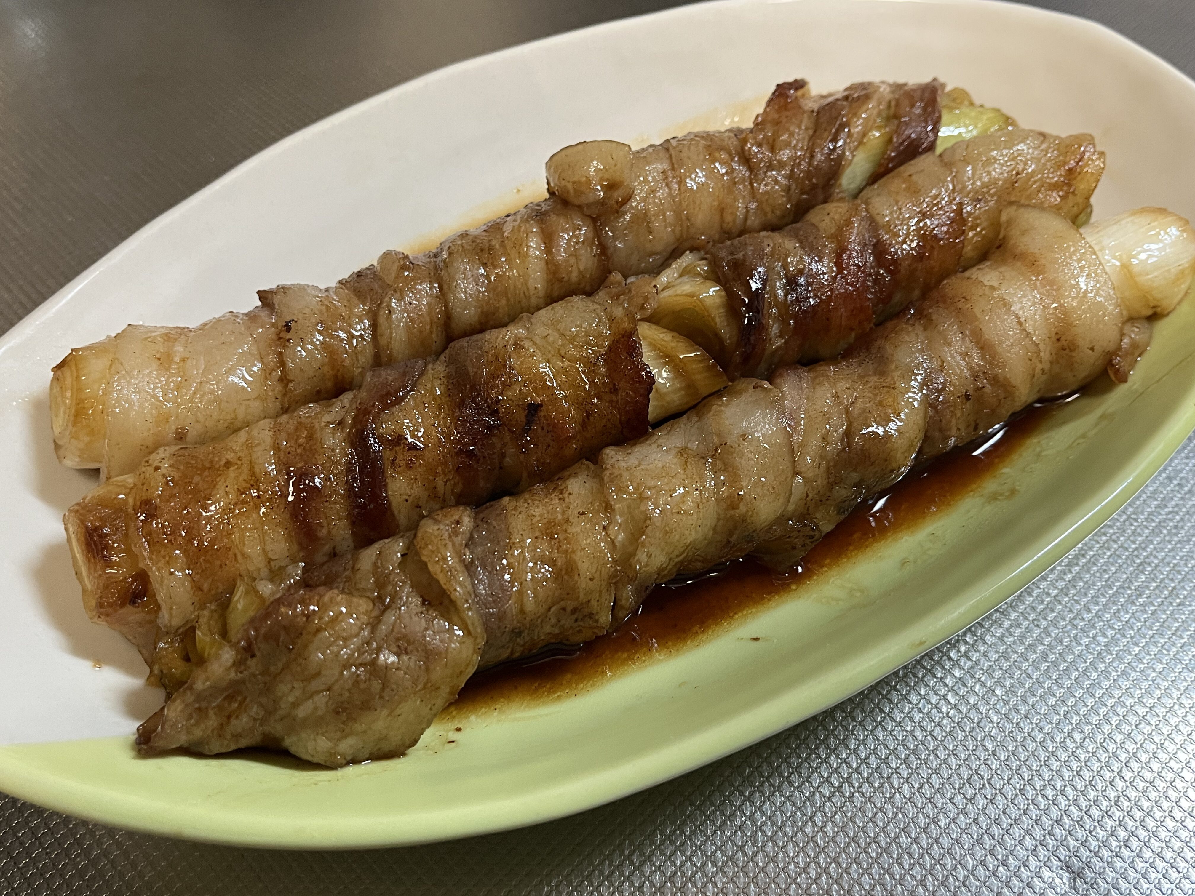 皿に盛り付けられた、豚肉で一本ネギを巻いて焼き、甘辛いタレを絡めたネギの肉巻き