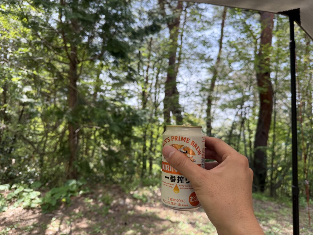 カーサイドタープの下から林間の景色を眺めながら手に持った缶ビールで乾杯している様子