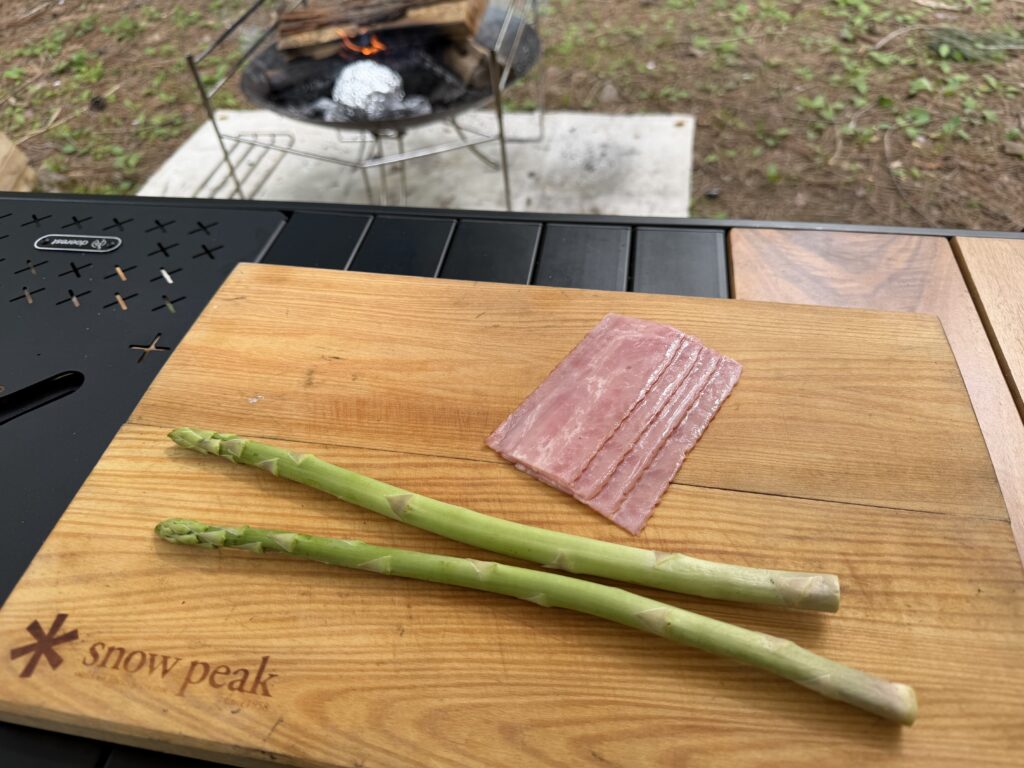 まな板の上にアスパラガスとベーコンが置かれ、おつまみの調理準備している様子