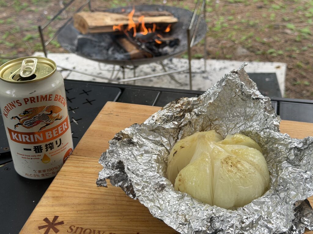 アルミホイルを開いた中に柔らかく火が通った新玉ねぎがあり、横にビールが置かれている様子