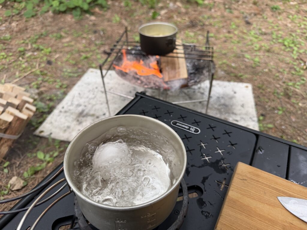 焚き火とバーナーを使って同時にジャガイモと卵を加熱し、ポテトサラダの下ごしらえをしている様子