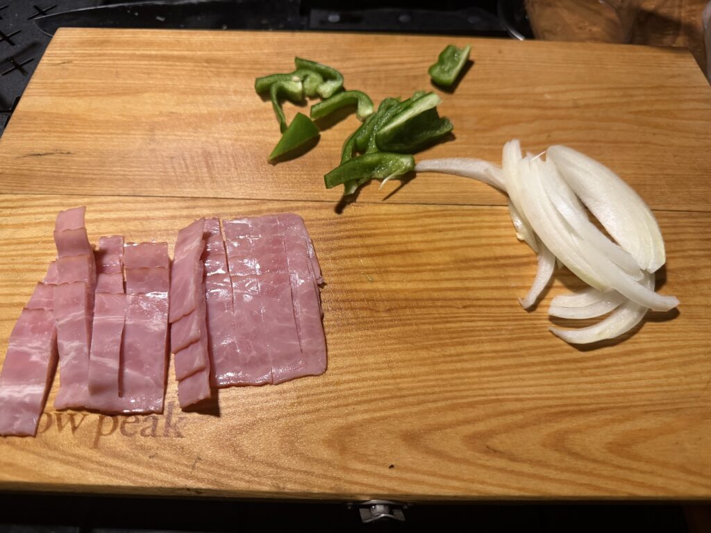 ピザの具材のベーコン、ピーマン、玉ねぎがカットされて、まな板の上に並べられている様子