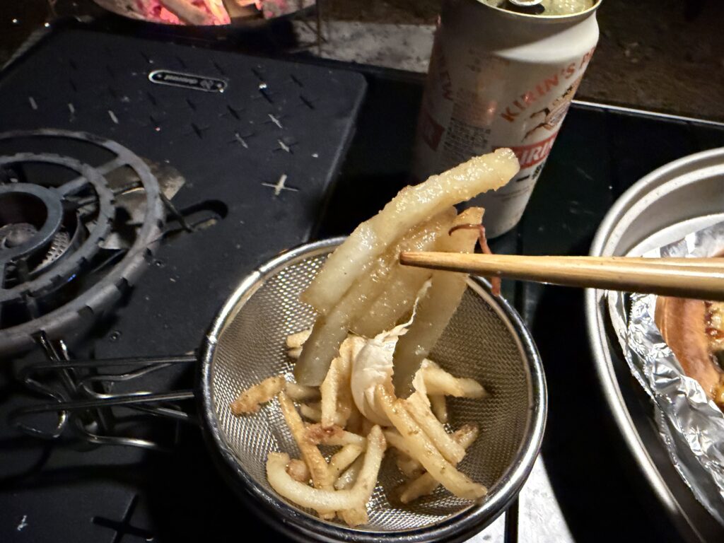 ホタルイカのアヒージョ油で揚げたフライドポテトを箸で持ち上げて食べようとしている様子