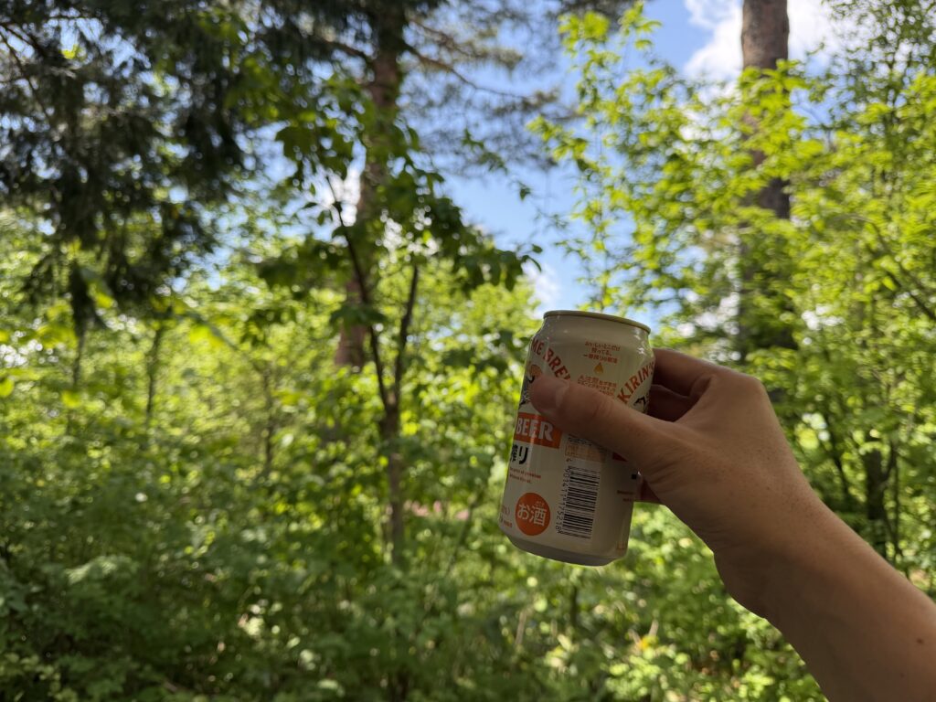 緑に囲まれた赤松サイトで、設営後に手に持った缶ビールを掲げている様子