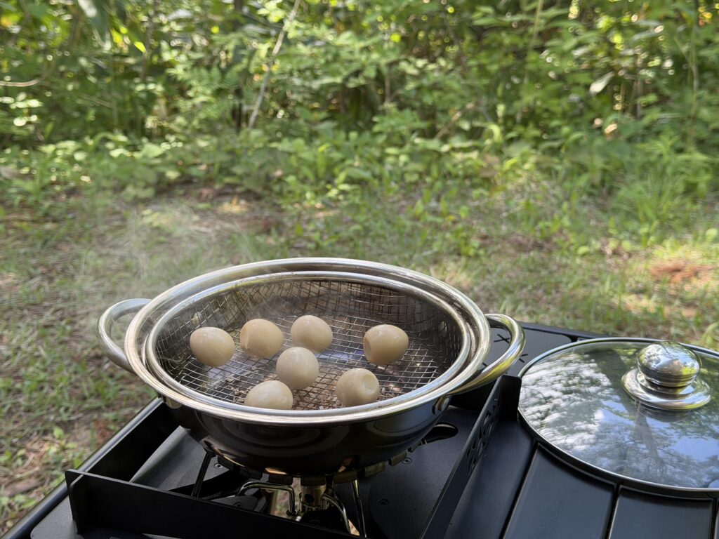 鍋で、うずらの卵を網に並べて燻製している様子。鍋の中から煙が出始めている。