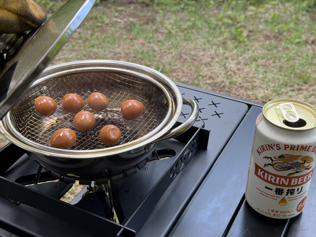 鍋の蓋を開け、茶色く色づいたうずらの卵の燻製と横に置いた缶ビールが写っている様子