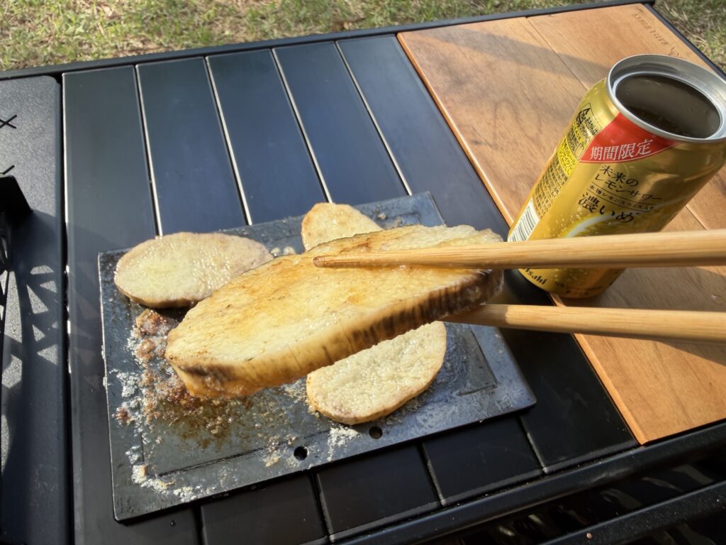 鉄板で焼いた長いもバター醤油焼きを箸で持ち上げ、横にレモンサワーの缶を置いて食べようとしている様子