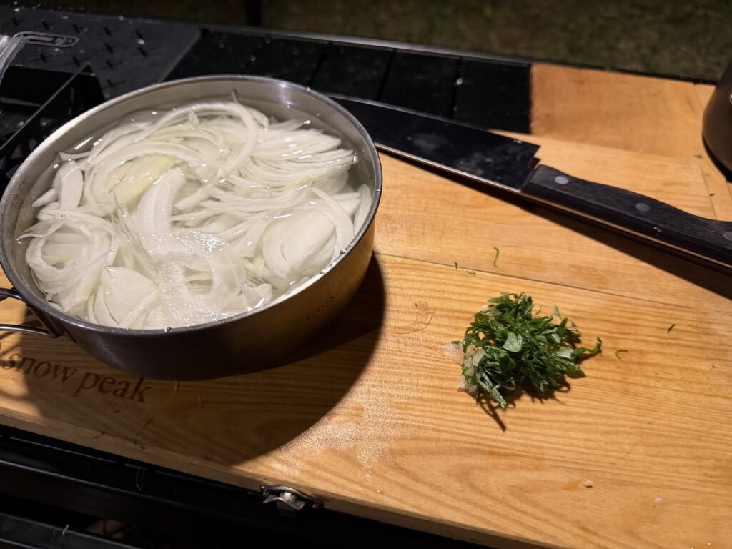 クッカーの水にさらしたスライス新玉ねぎと、まな板の上に刻んだ大葉を準備している様子