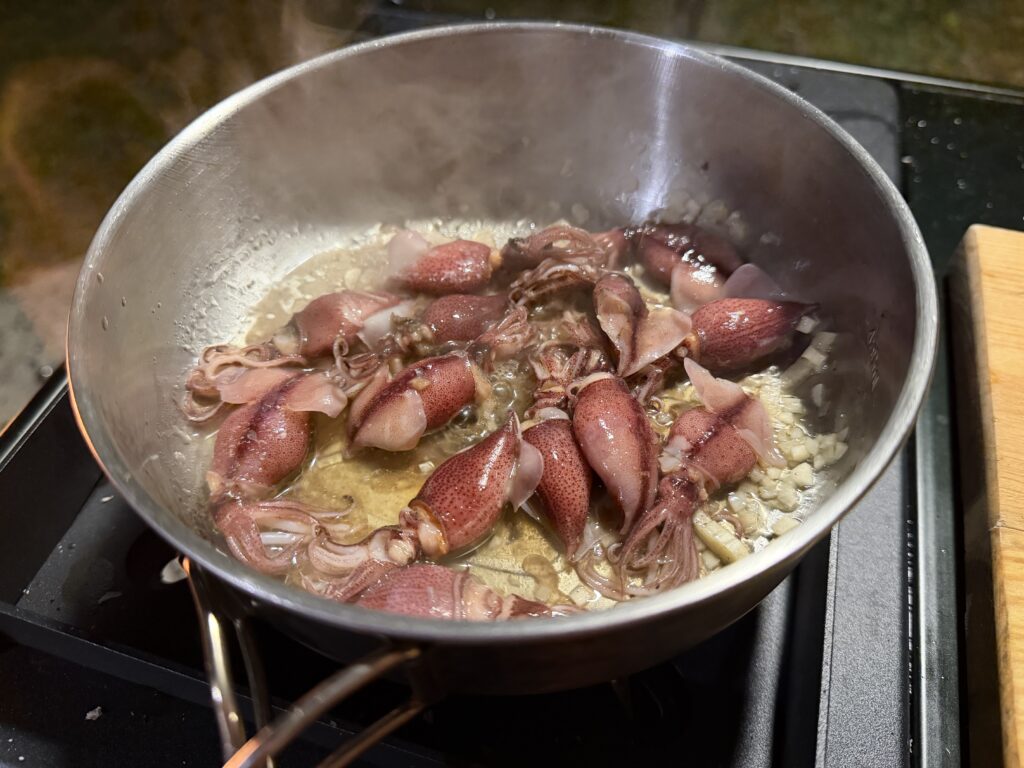 クッカーで刻んだニンニクとホタルイカをオリーブオイルで炒めている様子