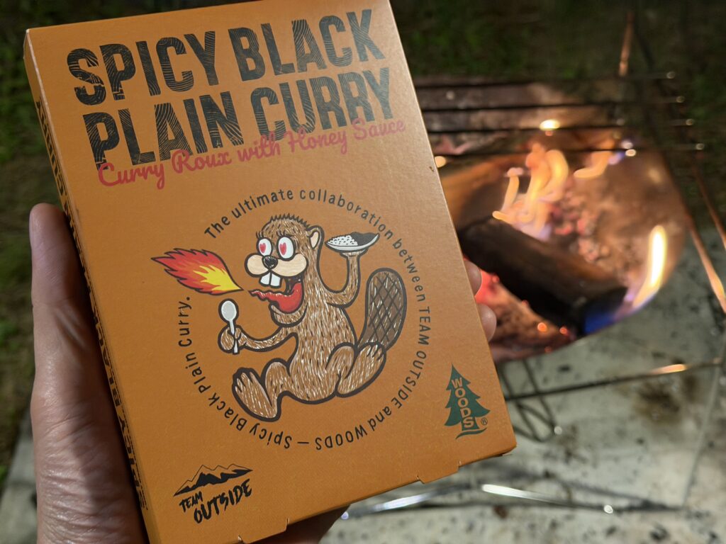 焚き火を背景に手に持ったSPICY BLACK PLAIN CURRYのパッケージ