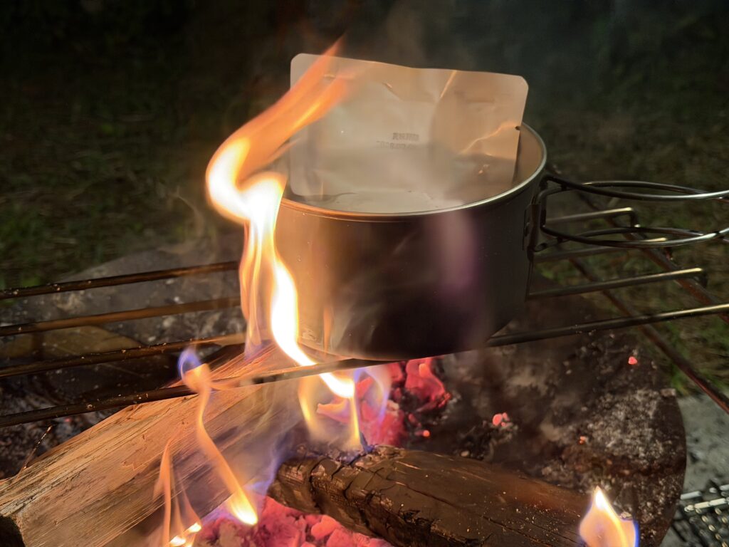 焚き火の強い炎で、クッカーに入れたレトルトカレーを温めている様子