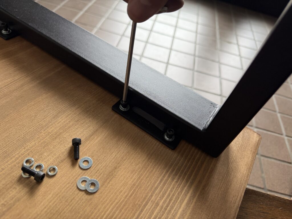 赤松集成材の天板に黒いロの字型テーブル脚をボルトで取り付けている様子