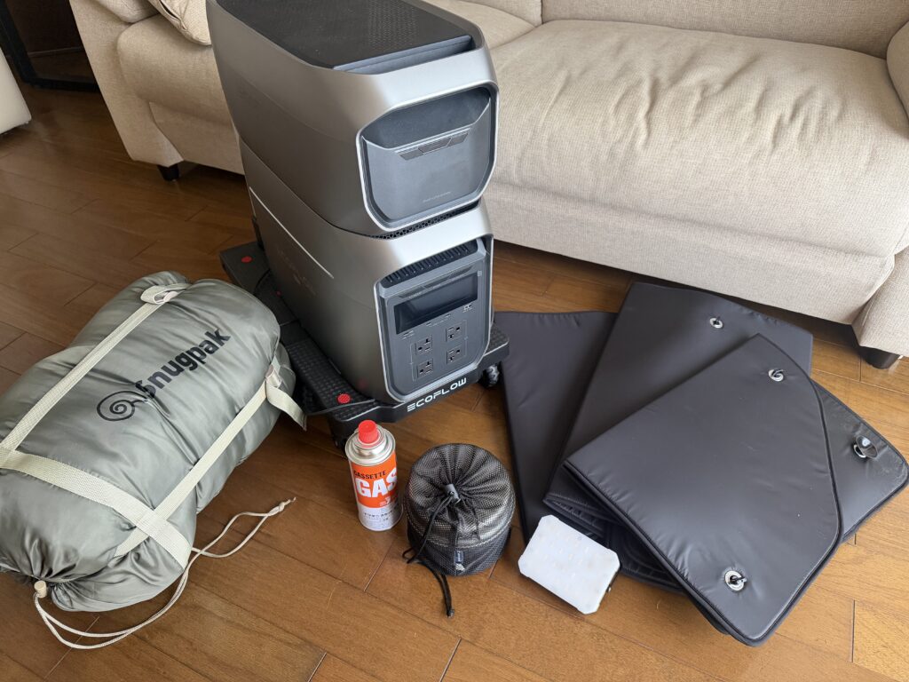 ポータブル電源や寝袋、サンシェード、ガス缶など車中泊と防災に使える道具を並べた写真