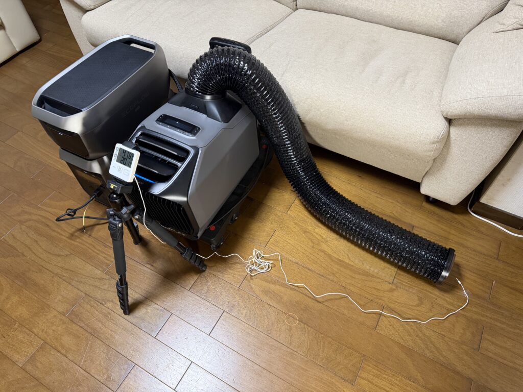 EcoFlow WAVE 3の排熱ダクトを本体から離すように長く伸ばし、リビングで試運転している様子。ポータブル電源と温度計も設置されている。