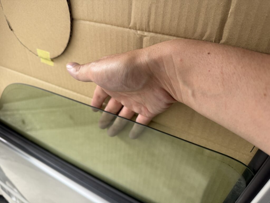 エブリイDA64Vの助手席窓に当てたダンボール型紙とガラスとの隙間を手で確認している様子。