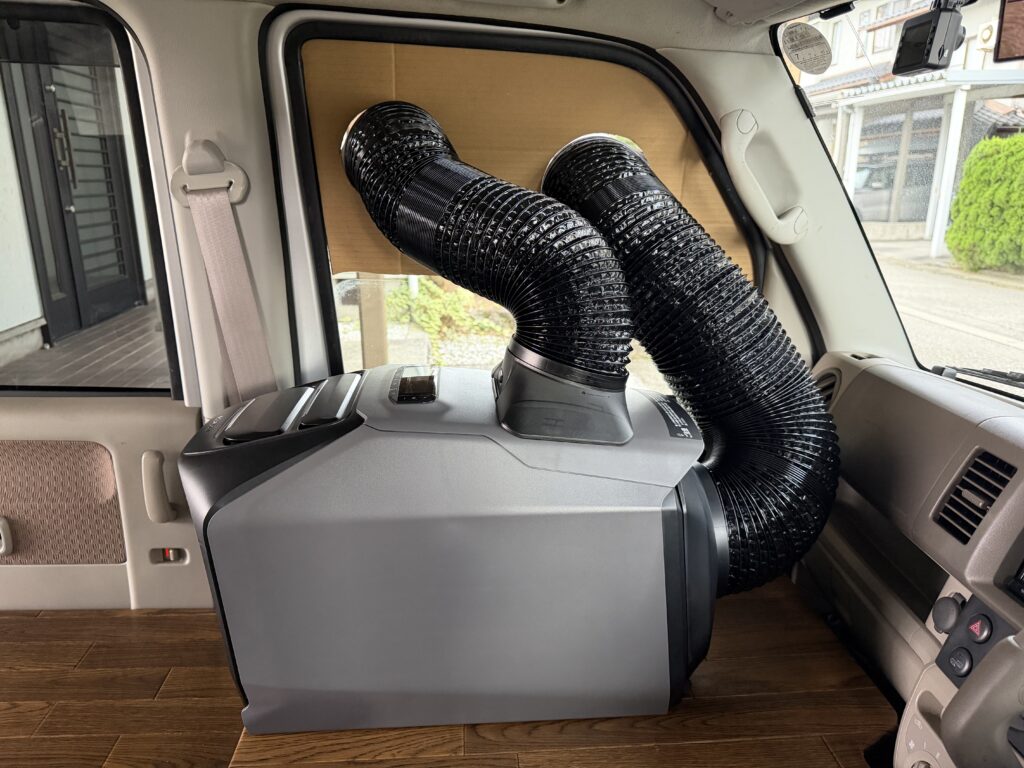EcoFlow WAVE 3本体から助手席窓のダンボール型紙へ、2本の黒いダクトを接続して車内側の取り回しを確認している様子。