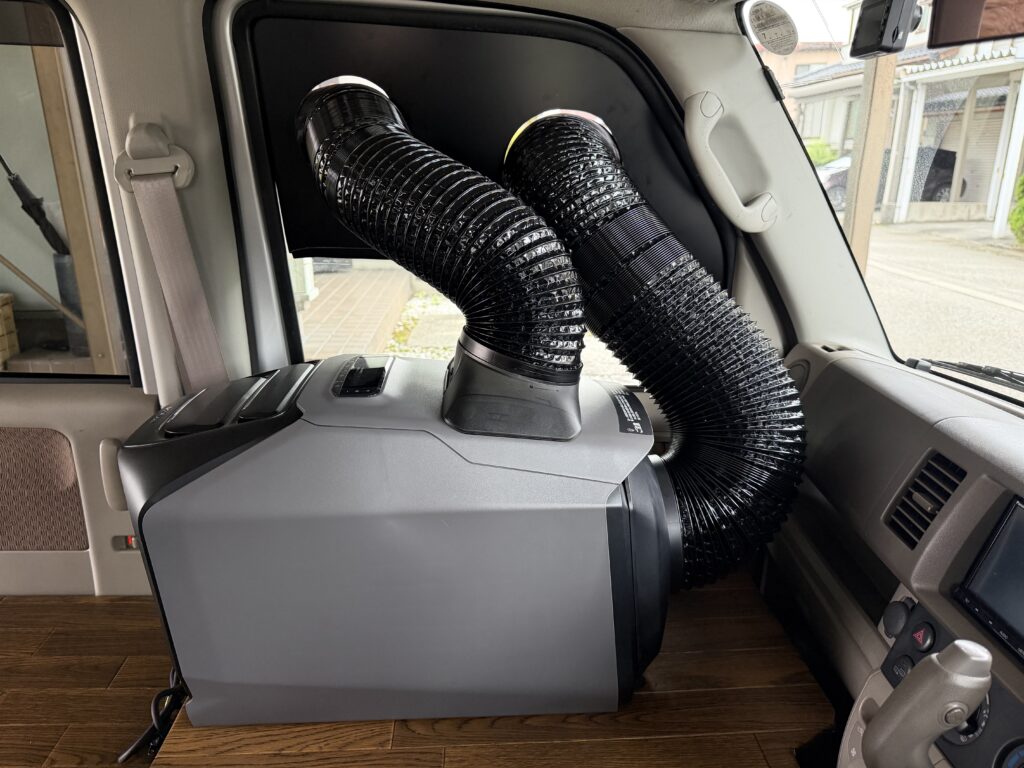 エブリイDA64Vの助手席側に置いたEcoFlow WAVE 3へ、窓パネルを通した2本のダクトを接続している車内側の様子