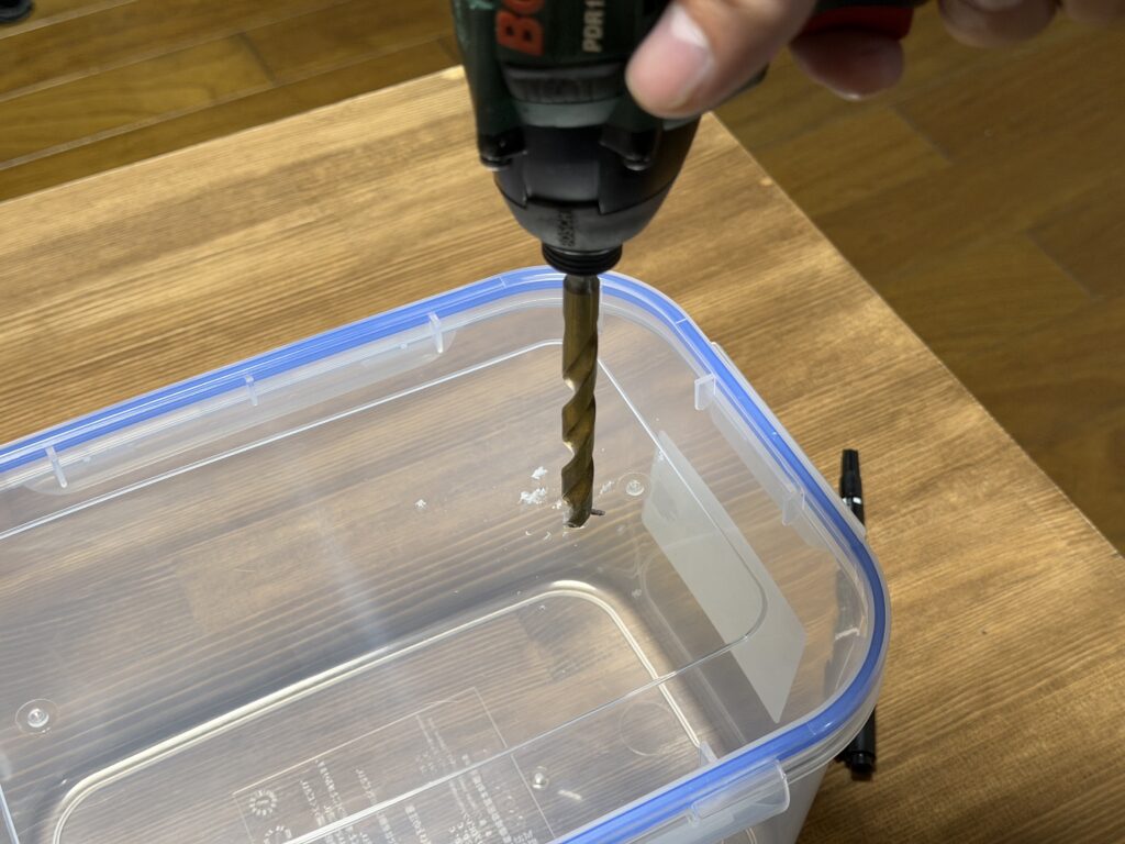 5Lの透明容器のフタに、ドリルで排水ホース用の穴を開けている様子