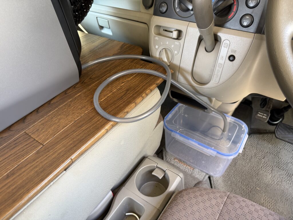 EcoFlow WAVE 3の排水ホースを5Lの透明容器へ接続し、車内へ設置した様子