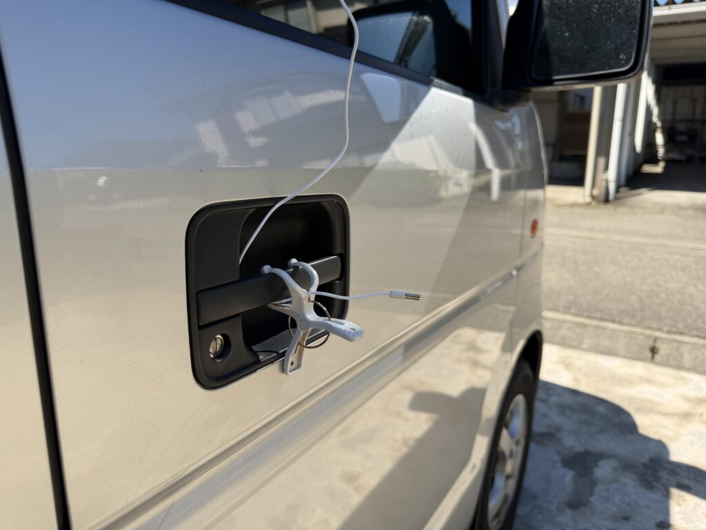 エブリイの運転席側ドアハンドルにクリップを取り付け、日陰で車外温度センサーを固定した様子