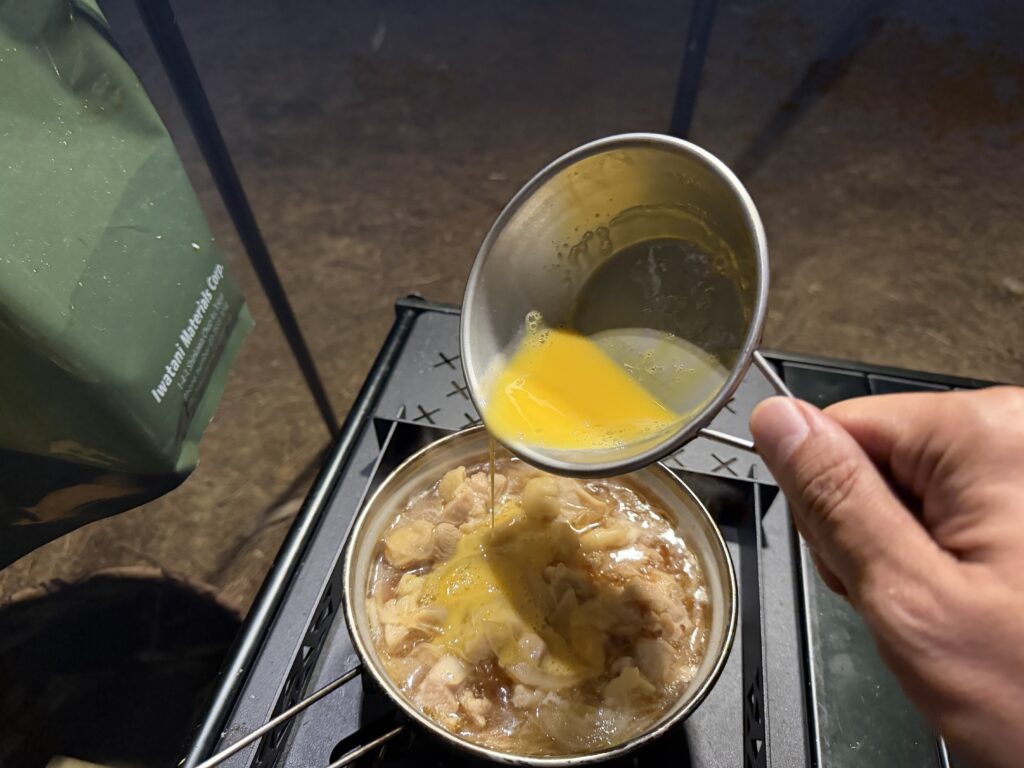 めんつゆで煮た鶏もも肉と玉ねぎの上へ溶き卵を回し入れる様子