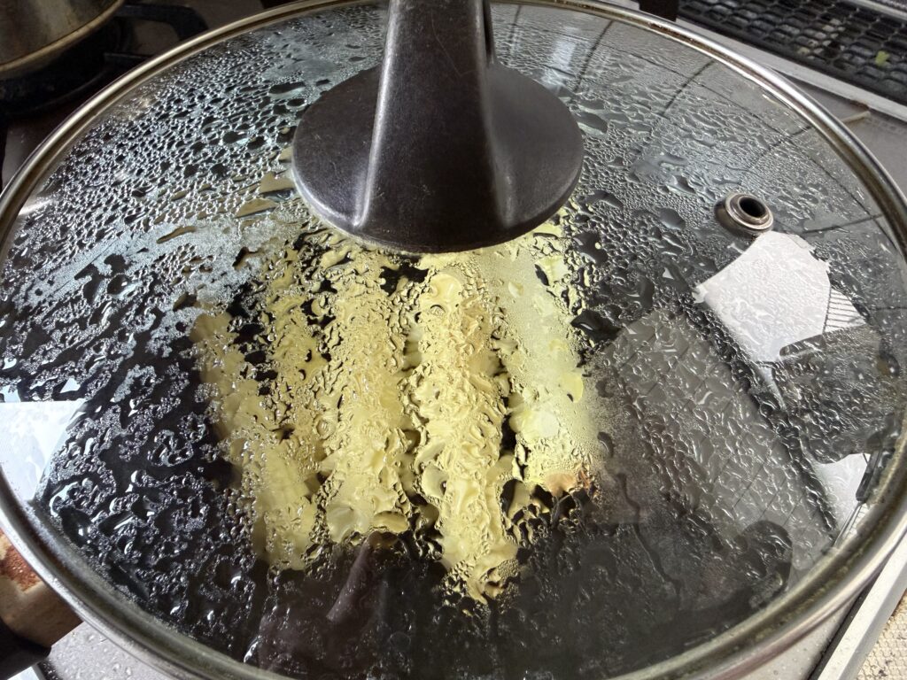 ヤングコーンを入れたフライパンに蓋をして蒸し焼きにしている様子