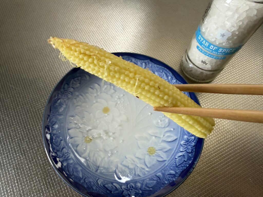 蒸し焼きにした自家栽培ヤングコーンへ塩を振って味見している様子