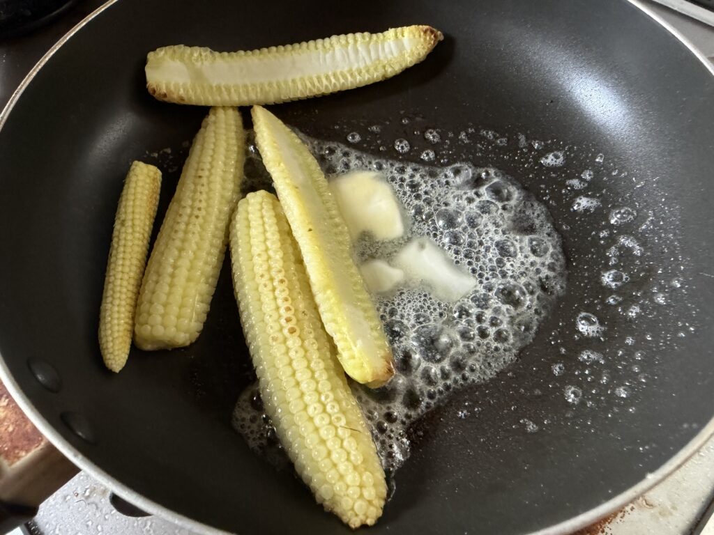 蒸し焼きにしたヤングコーンへバターを加えている様子