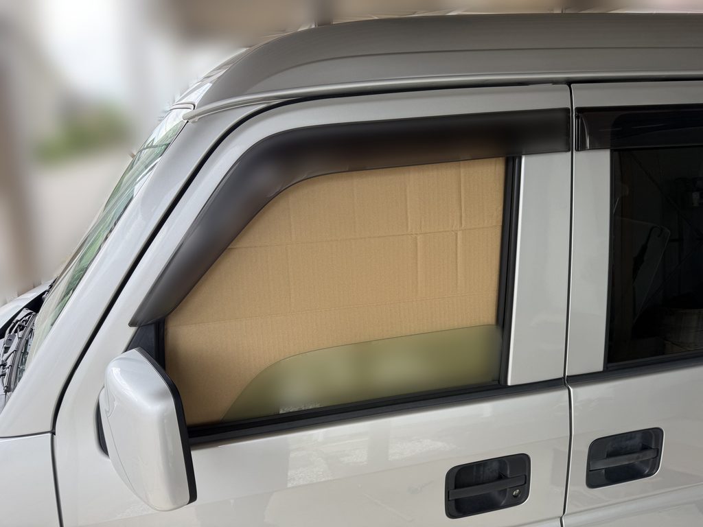 エブリイDA64Vの助手席窓にダンボール型紙を仮固定し、車外側からサイズを確認している様子。