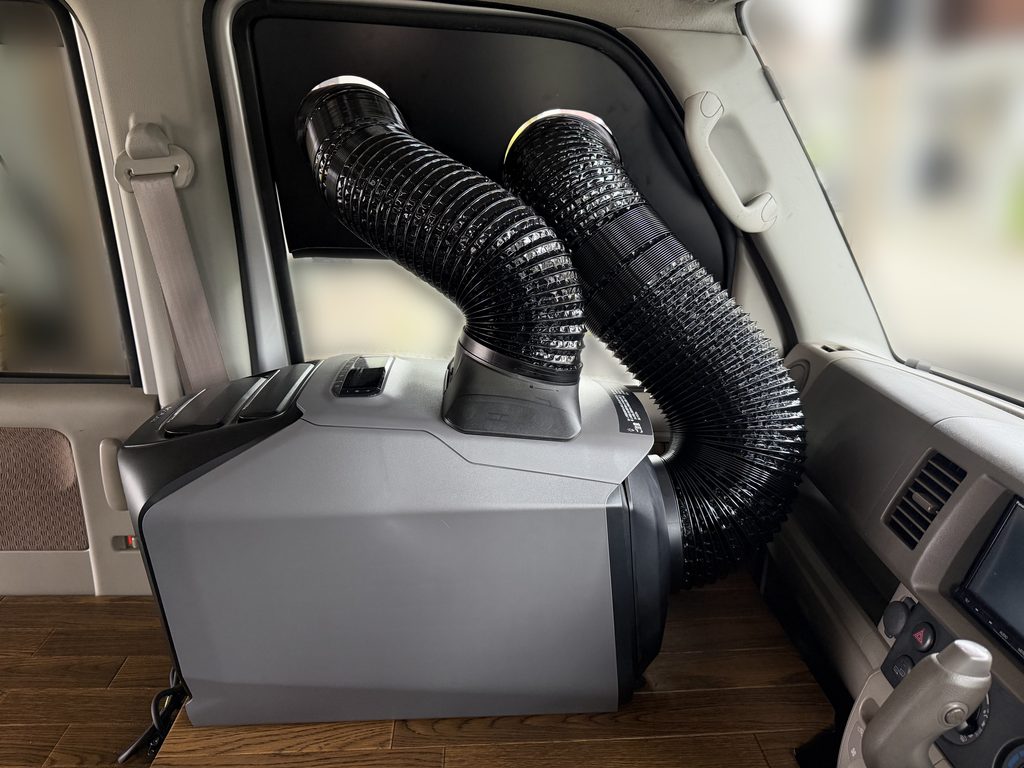 エブリイDA64Vの助手席側に置いたEcoFlow WAVE 3へ、窓パネルを通した2本のダクトを接続している車内側の様子
