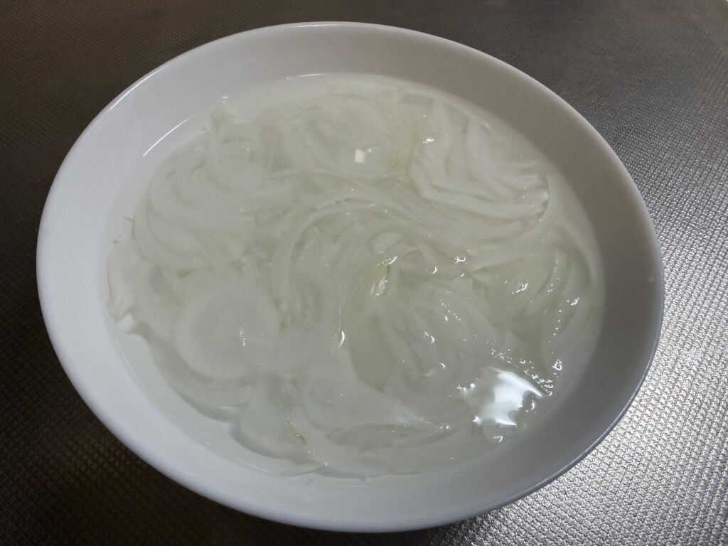 薄くスライスした玉ねぎを白い器の水にさらしている様子
