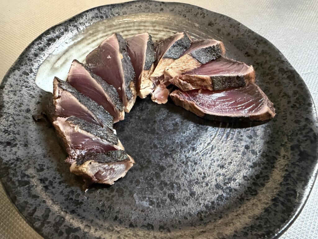 厚切りにしたカツオのたたきを黒い皿に並べた様子