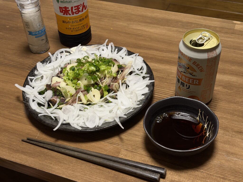 薬味をたっぷりのせたカツオのたたきをポン酢と塩、ビールと一緒に食卓へ並べた様子