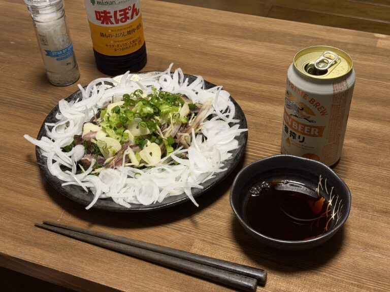 薬味をたっぷりのせたカツオのたたきをポン酢と塩、ビールと一緒に食卓へ並べた様子