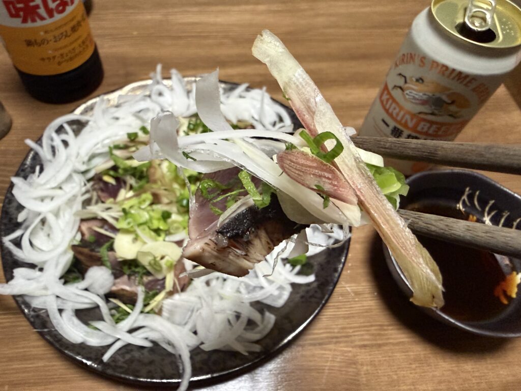 薬味をたっぷりのせたカツオのたたきを箸で持ち上げている様子