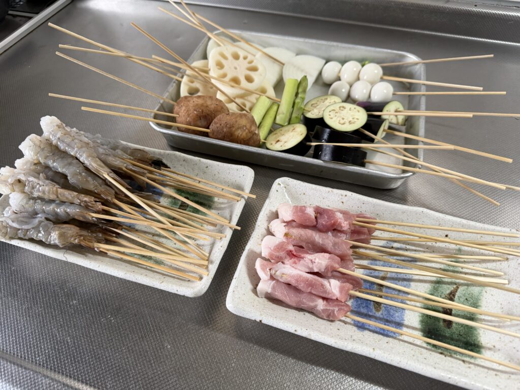 エビ、豚肉、ナス、オクラ、れんこん、うずら卵などを串に刺して皿に並べた様子