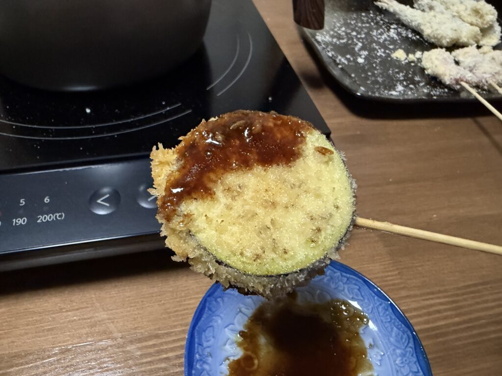家庭菜園で収穫したナスを輪切りにして串揚げにし、ソースをかけた様子