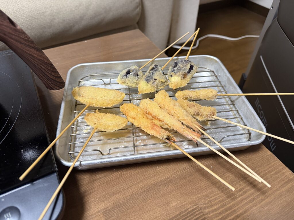 揚げたエビ、ナス、たまねぎなどの串揚げをバットの網に並べた様子