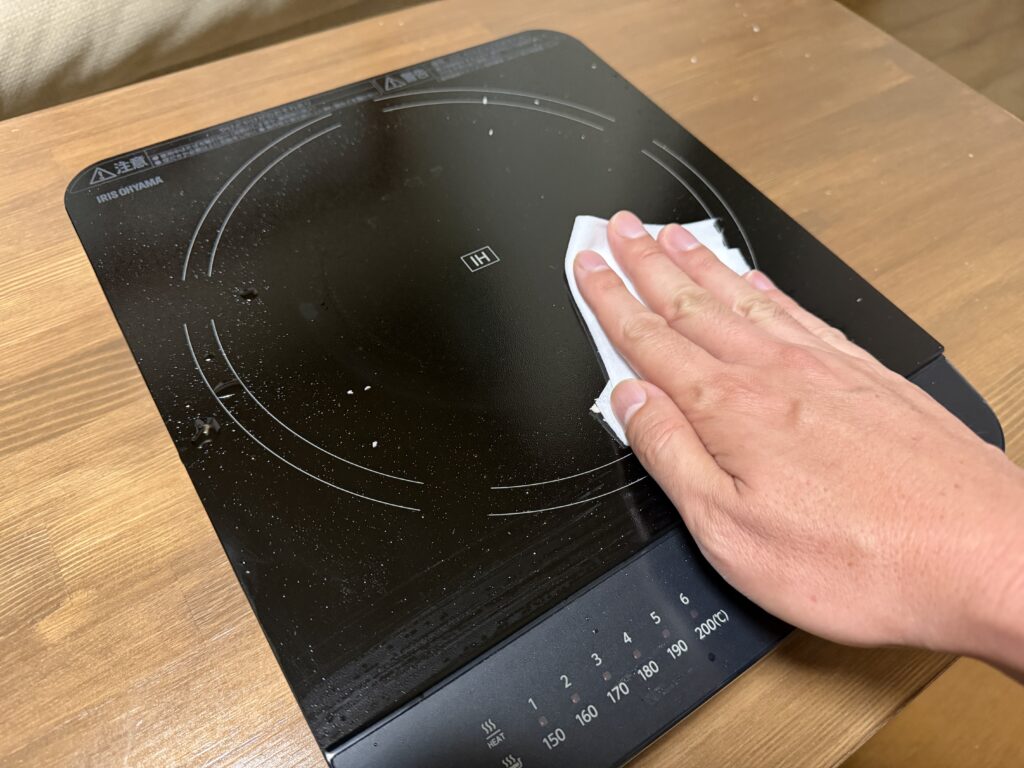 アルコールタイプのウェットティッシュでIHコンロの天板を拭いている様子