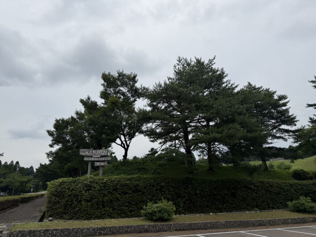 曇り空の下に立つ閑乗寺公園キャンプ場の入口看板と周囲の緑