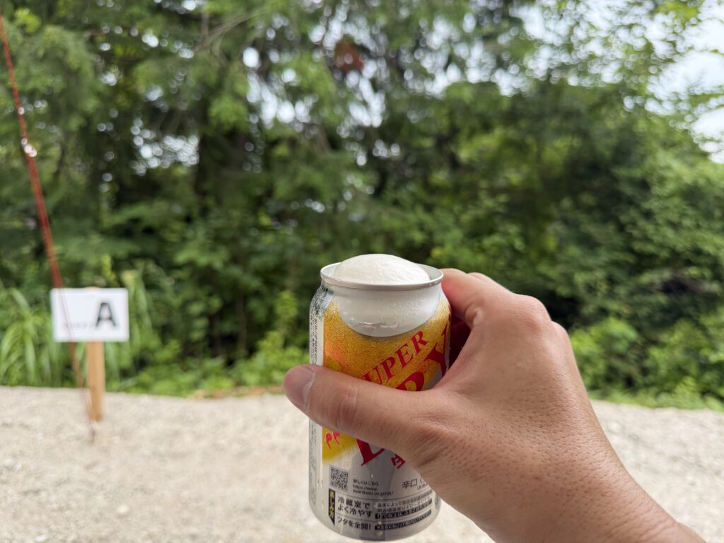 緑に囲まれた閑乗寺公園キャンプ場のソロエリアで、缶ビールを手に乾杯する様子