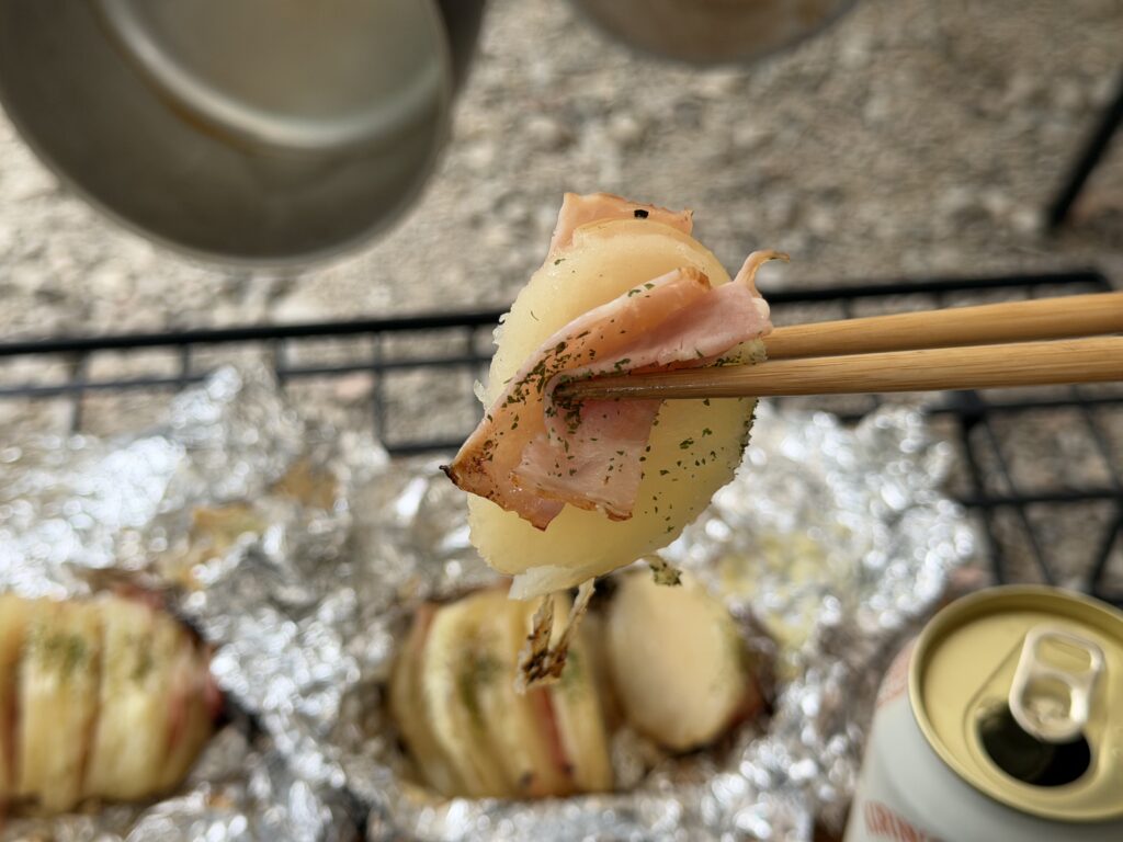 ベーコンとチーズが見えるハッセルバックポテトを箸で持ち上げた様子