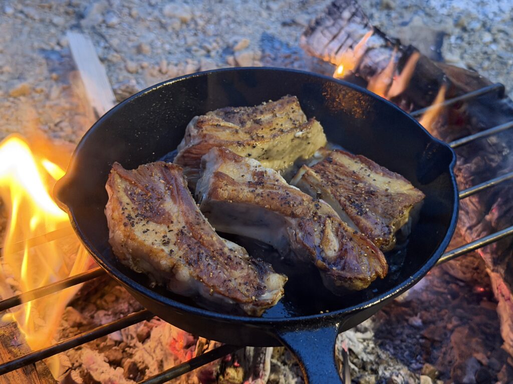 直火にかけたスキレットで表面を香ばしく焼いている豚スペアリブ