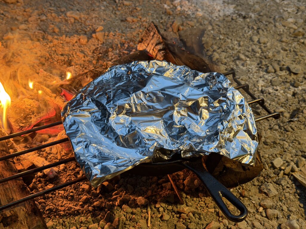 弱火ゾーンへ移し、アルミホイルをかぶせてスペアリブを蒸し焼きにしているスキレット